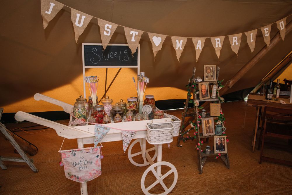 Rustic wedding candy cart with bunting and decorative displays inside a tent venue.