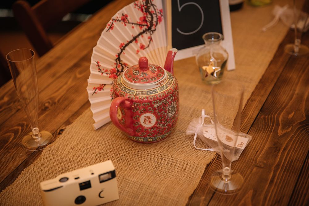 Red decorated jar centerpiece with disposable camera and table number on wooden surface.