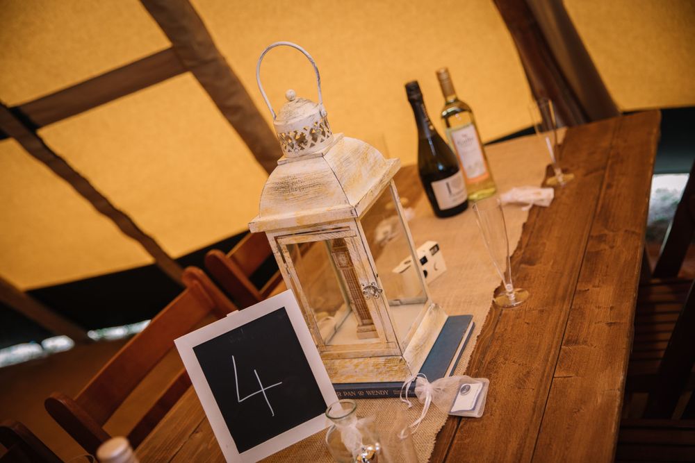 White lantern and wine bottle displayed on rustic wooden table with small chalkboard number sign.