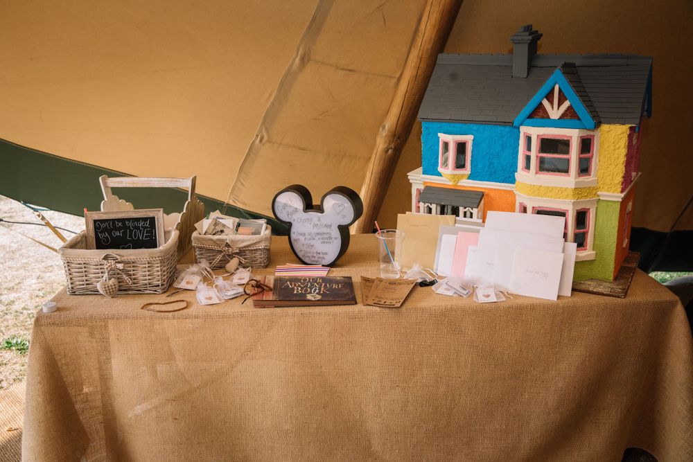Wedding decor display featuring miniature blue dollhouse and Mickey Mouse themed items on tan tablecloth.