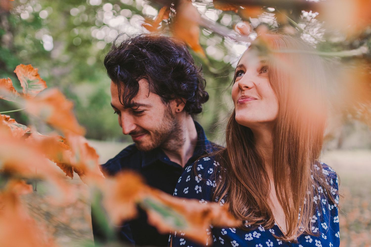 A couple shares an intimate moment framed by blurred orange autumn foliage.