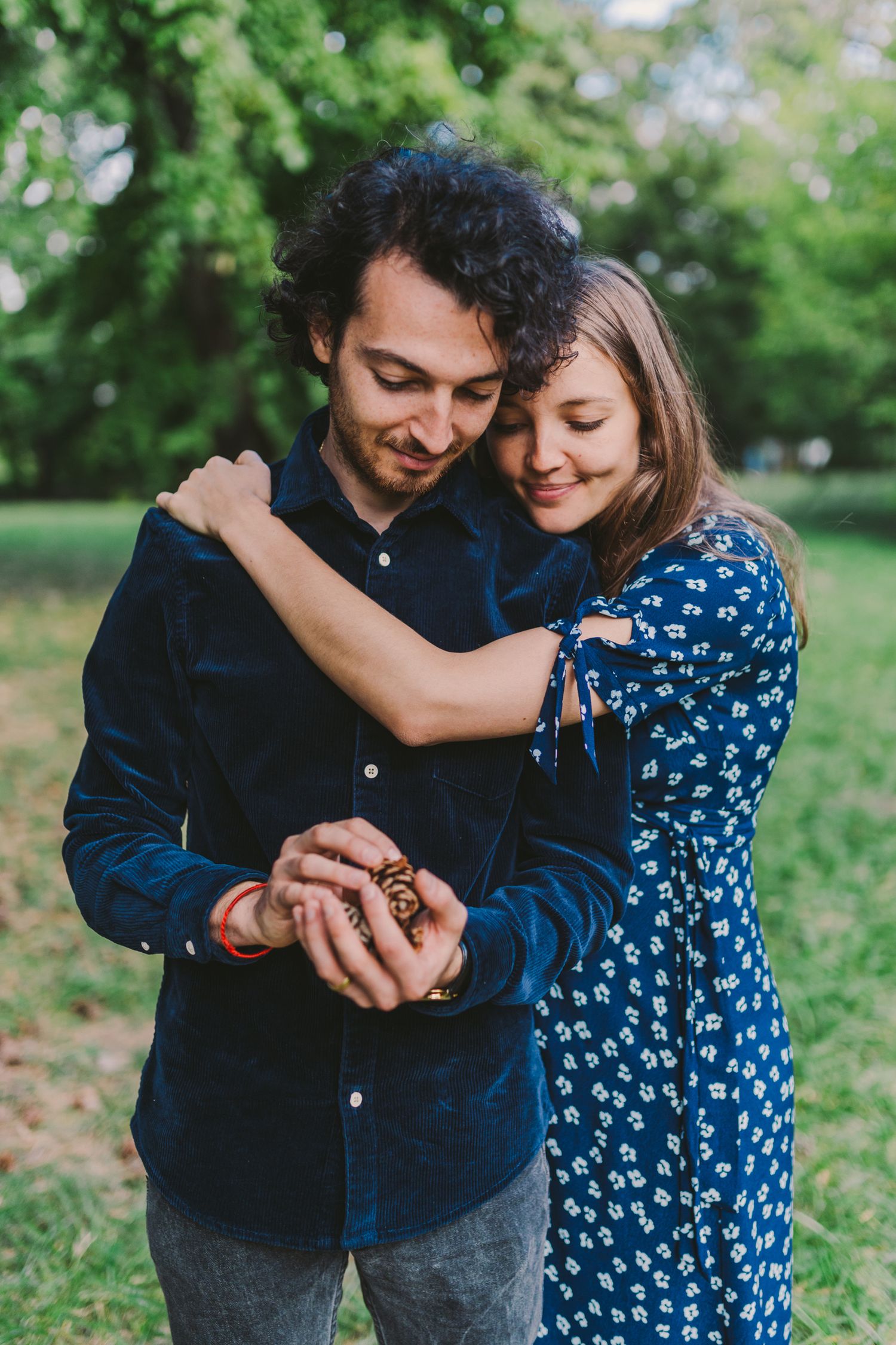 A couple embraces while examining something in their hands in a green park setting.