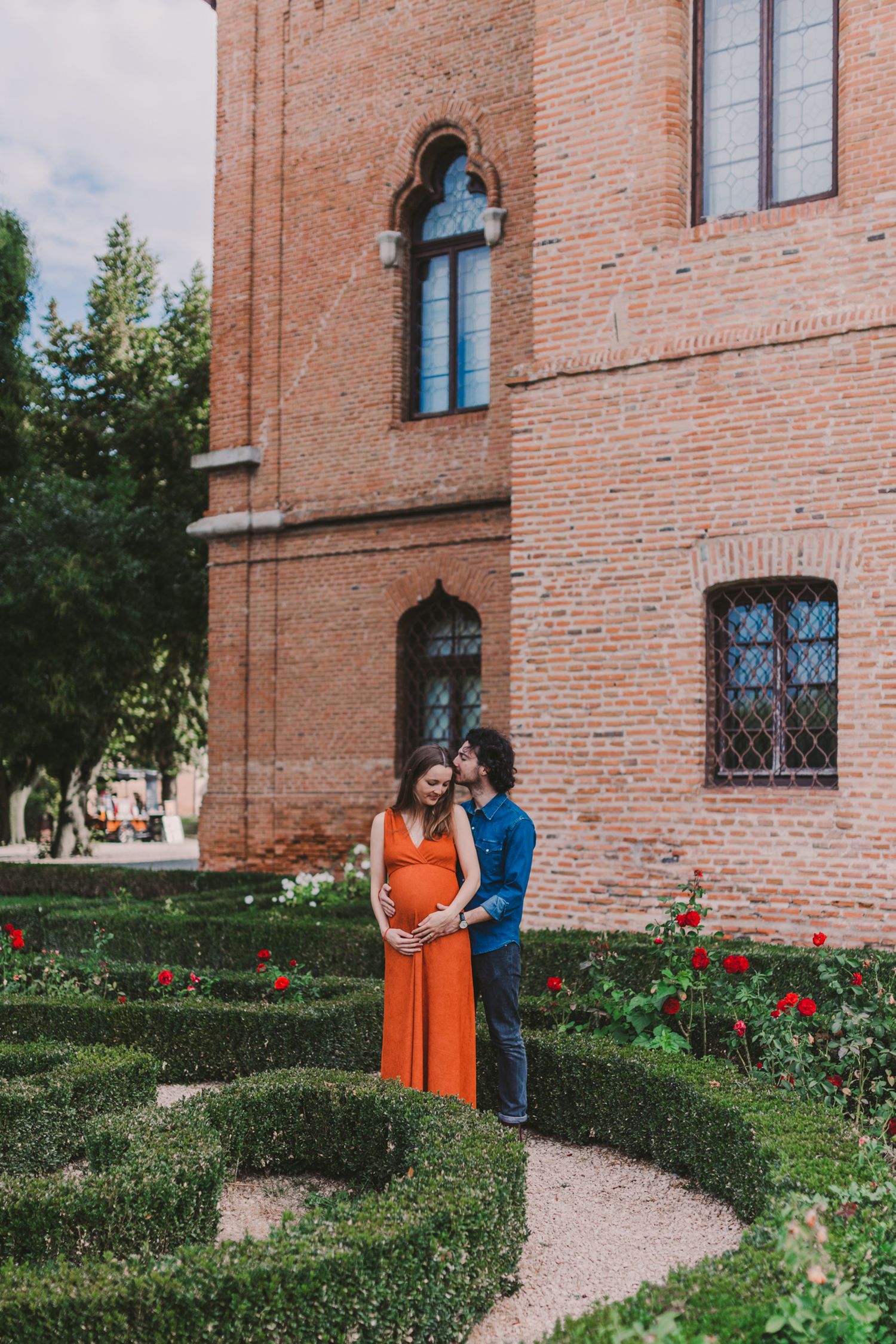 Maternity photography session in front of historic building with manicured gardens.
