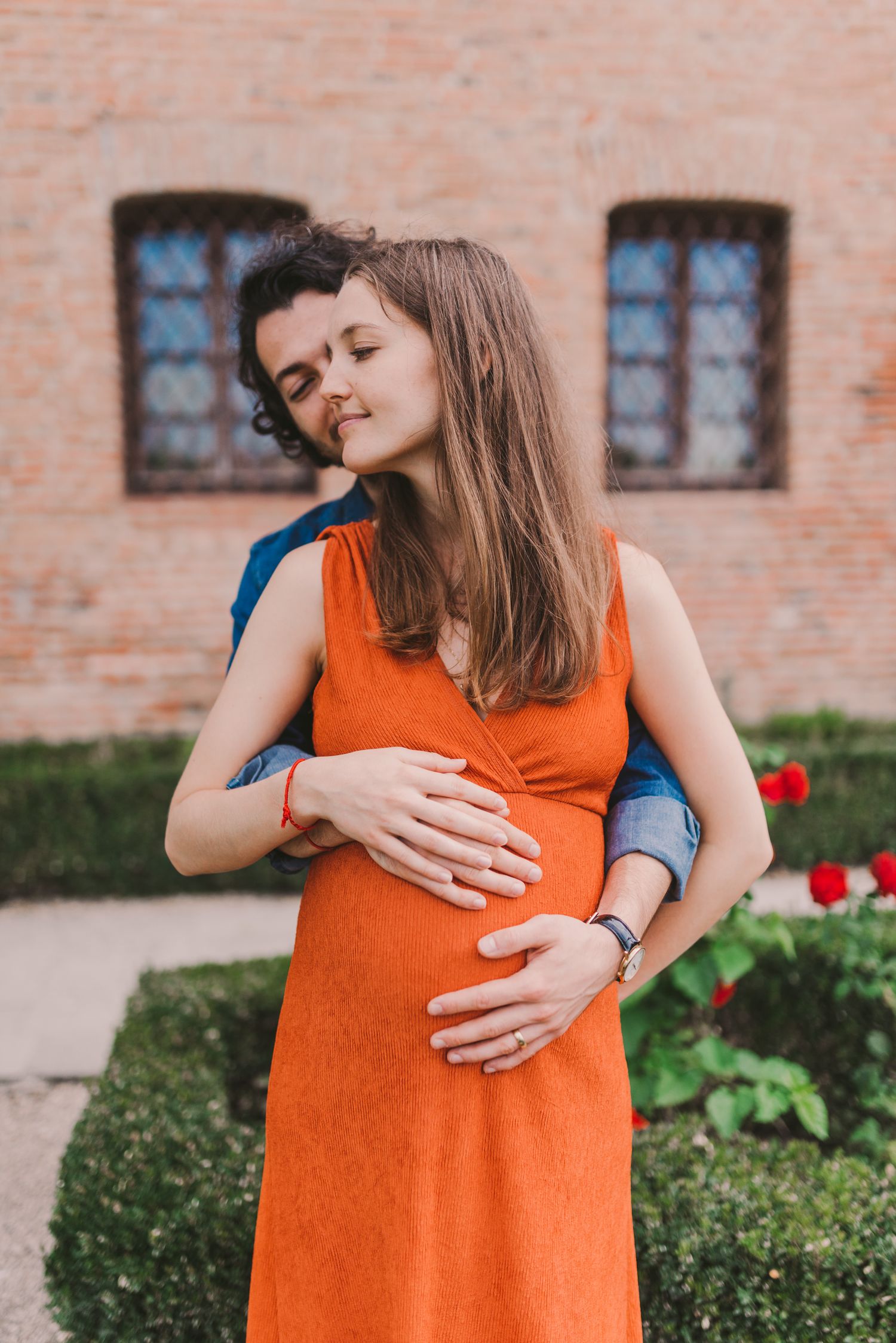 Close-up shots of pregnancy photoshoot with orange dress against brick wall.