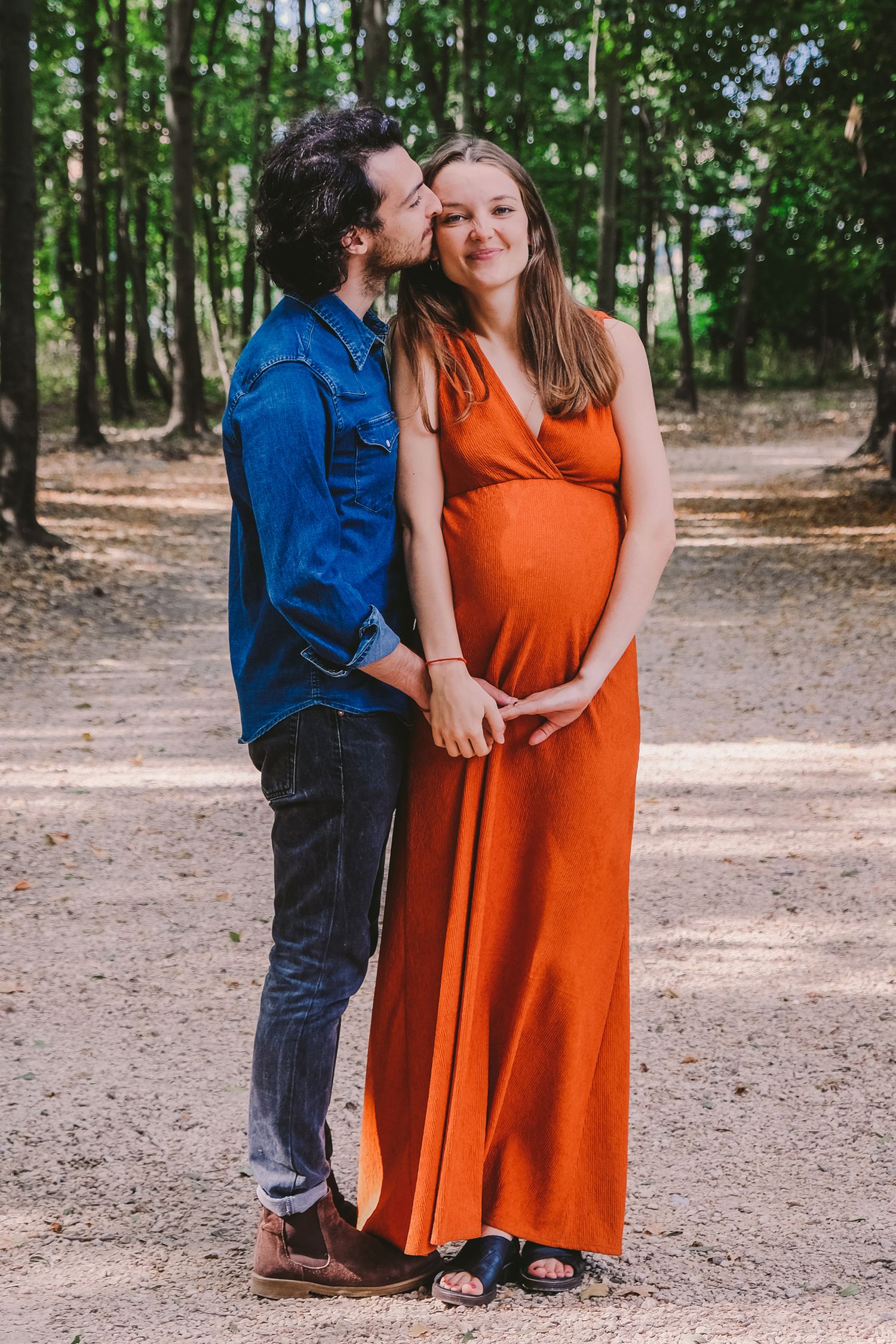 Outdoor maternity session in wooded area with couple in orange dress and denim.