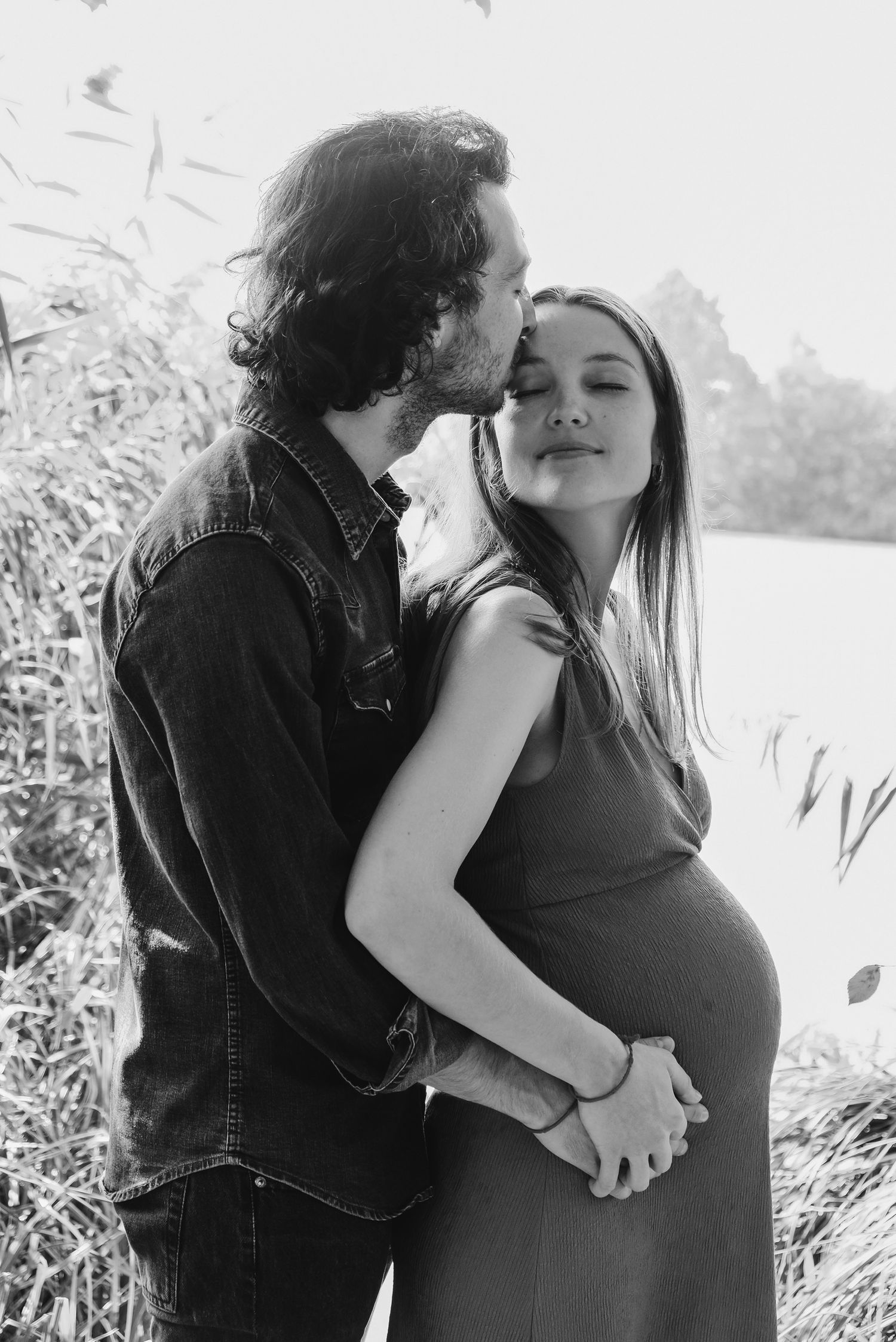 Black and white intimate portraits of a couple embracing outdoors near water and reeds.