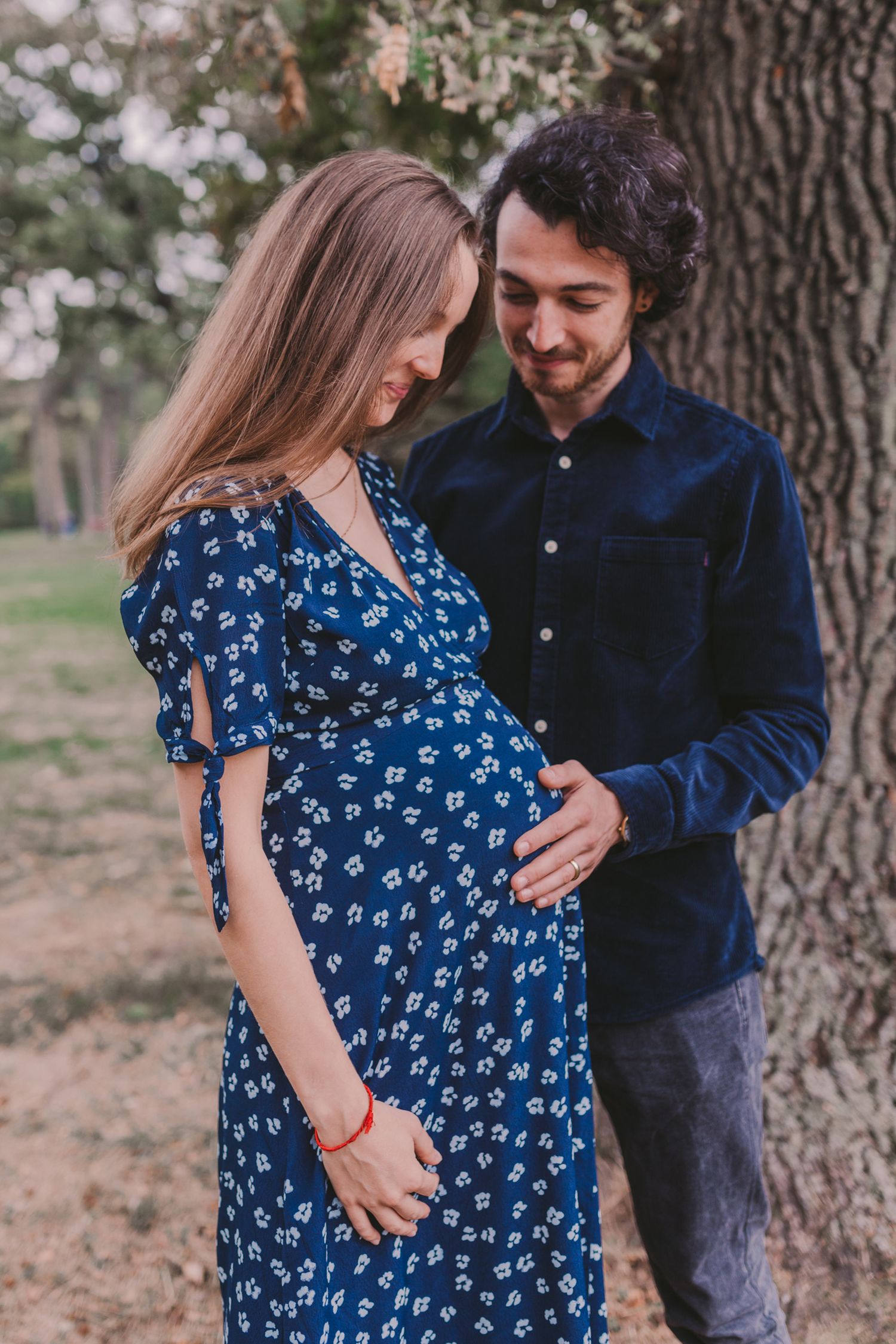 Couple in blue and navy clothing sharing intimate moments by a tree.