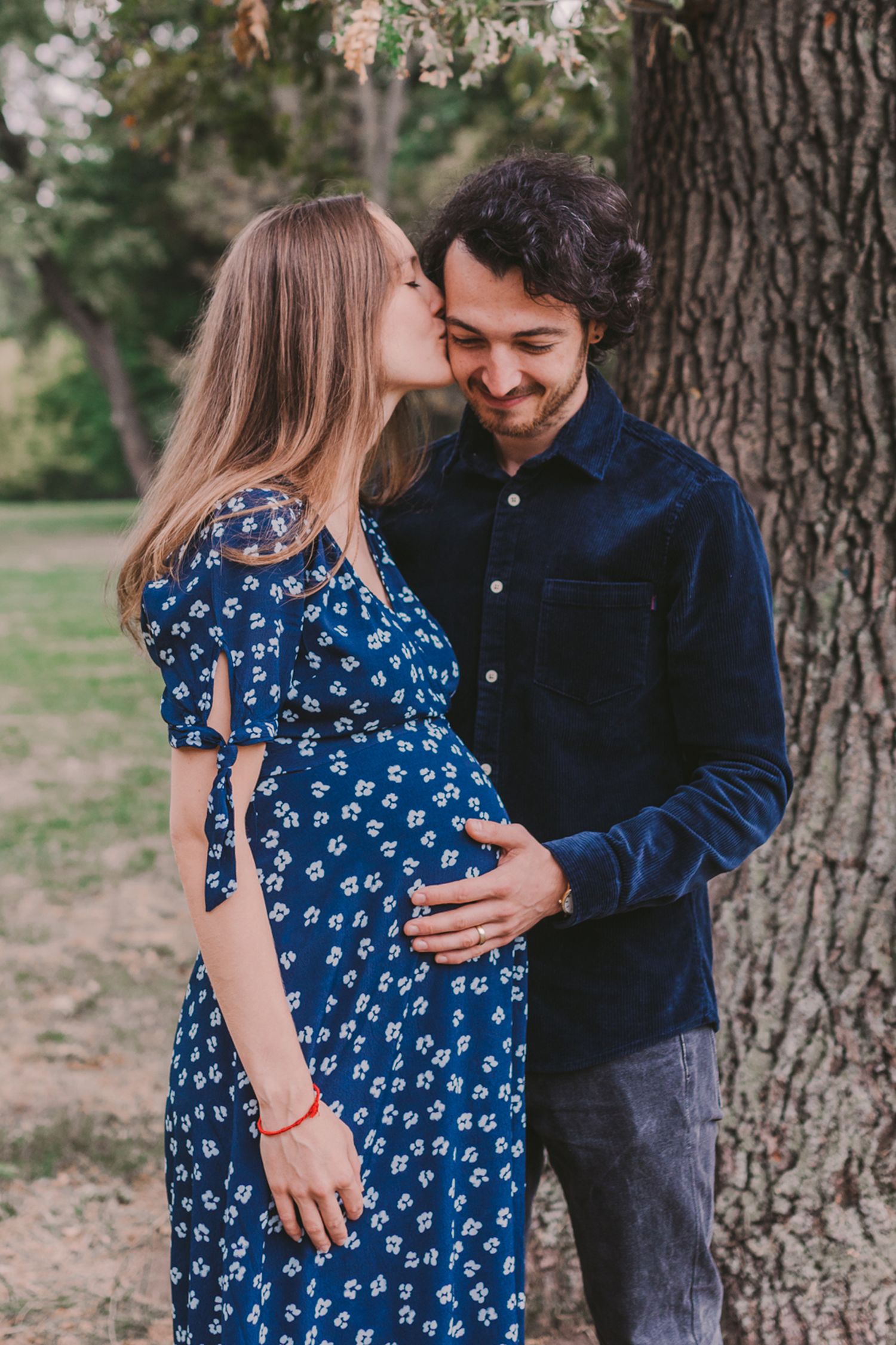 Couple embracing outdoors near a large tree trunk in a natural setting.