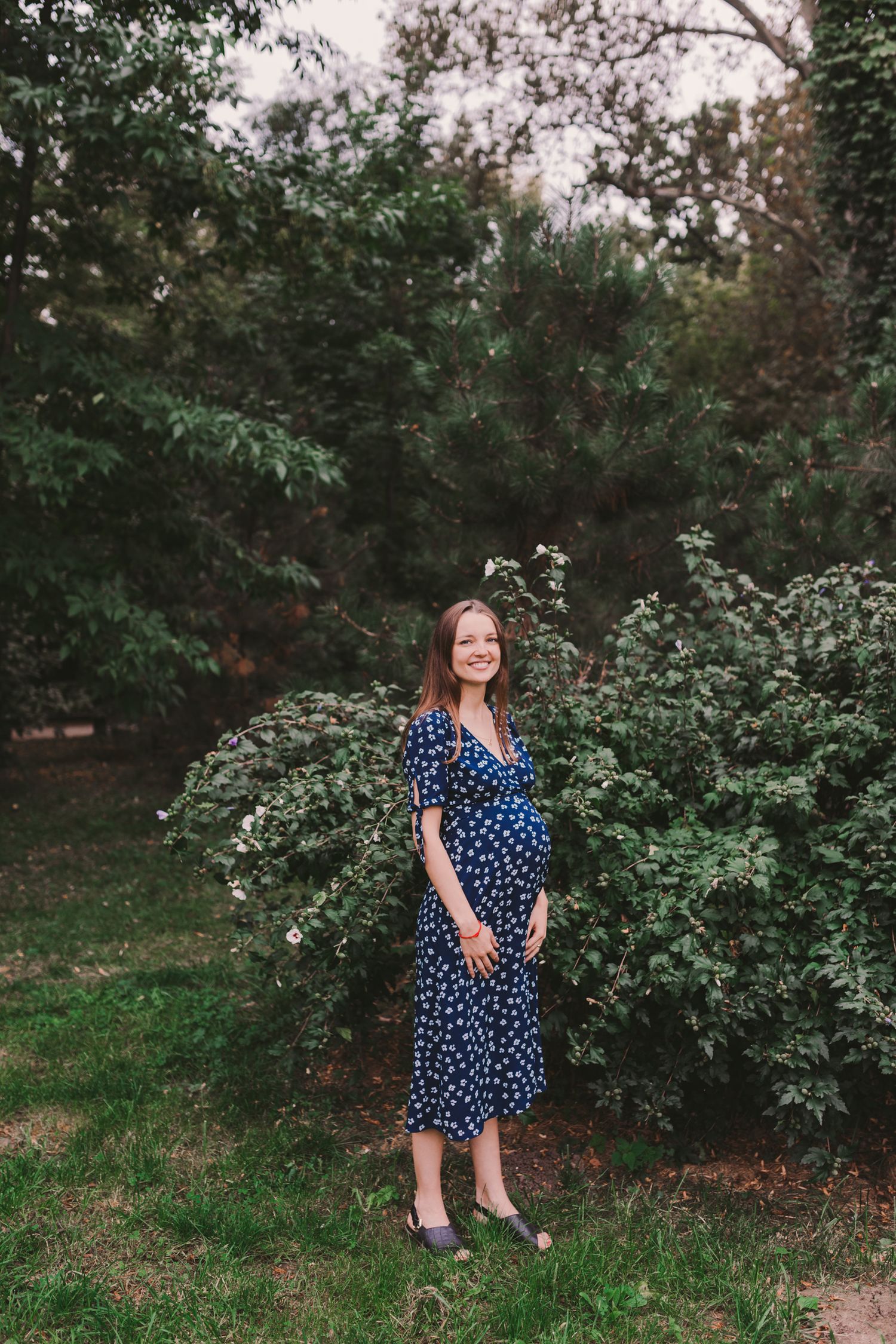 Woman in blue floral dress standing in a garden setting.