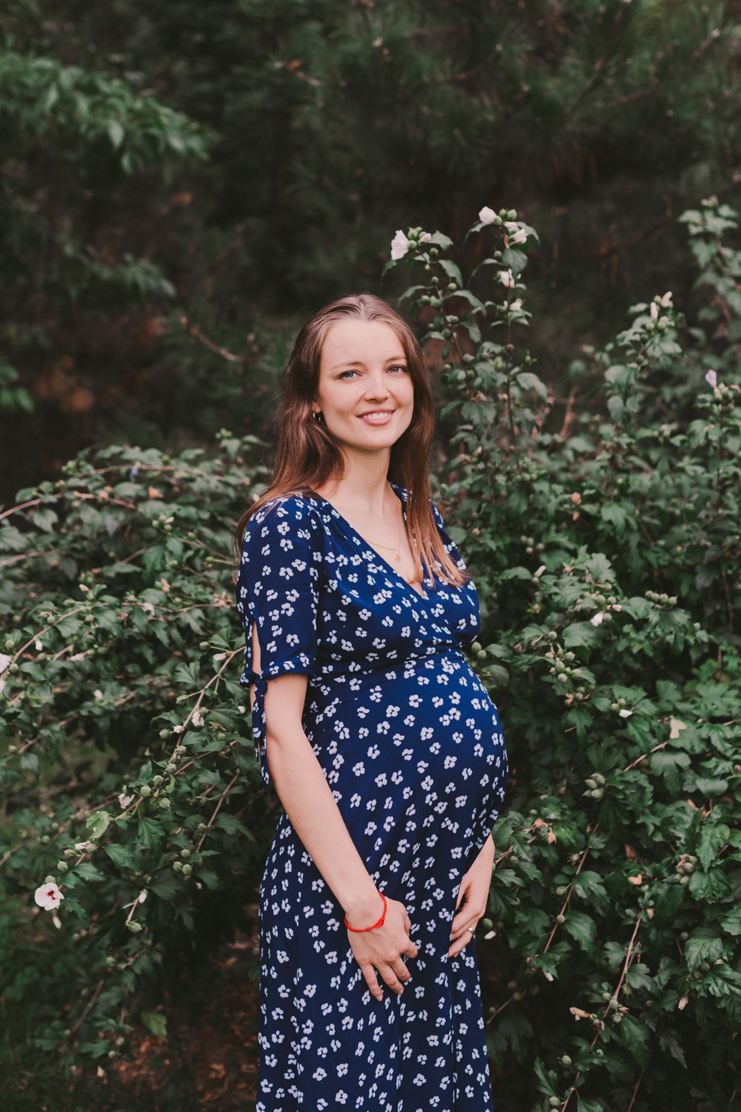 Woman in patterned blue dress posing in front of green foliage.