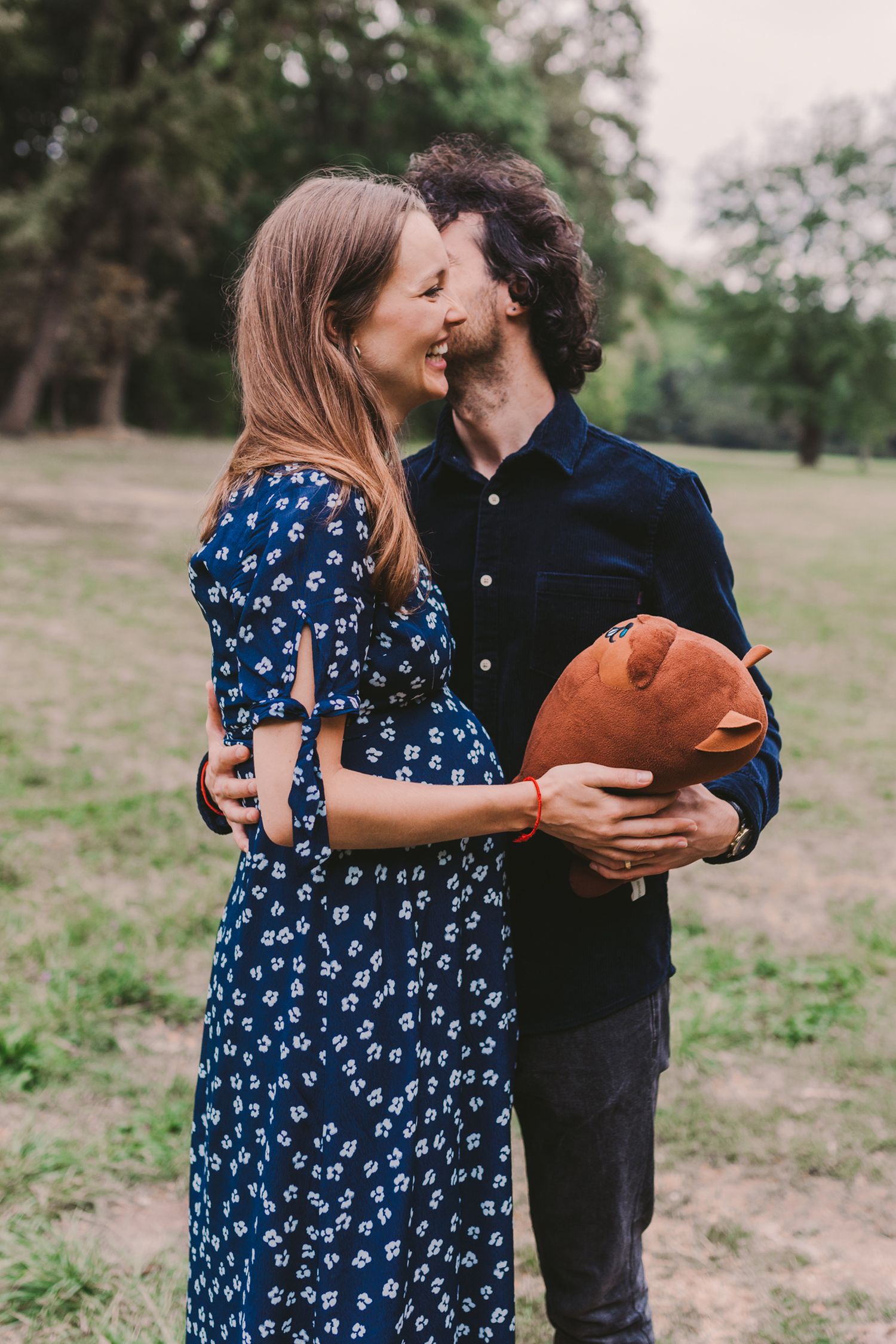 A couple shares a playful moment with a teddy bear in an outdoor setting.