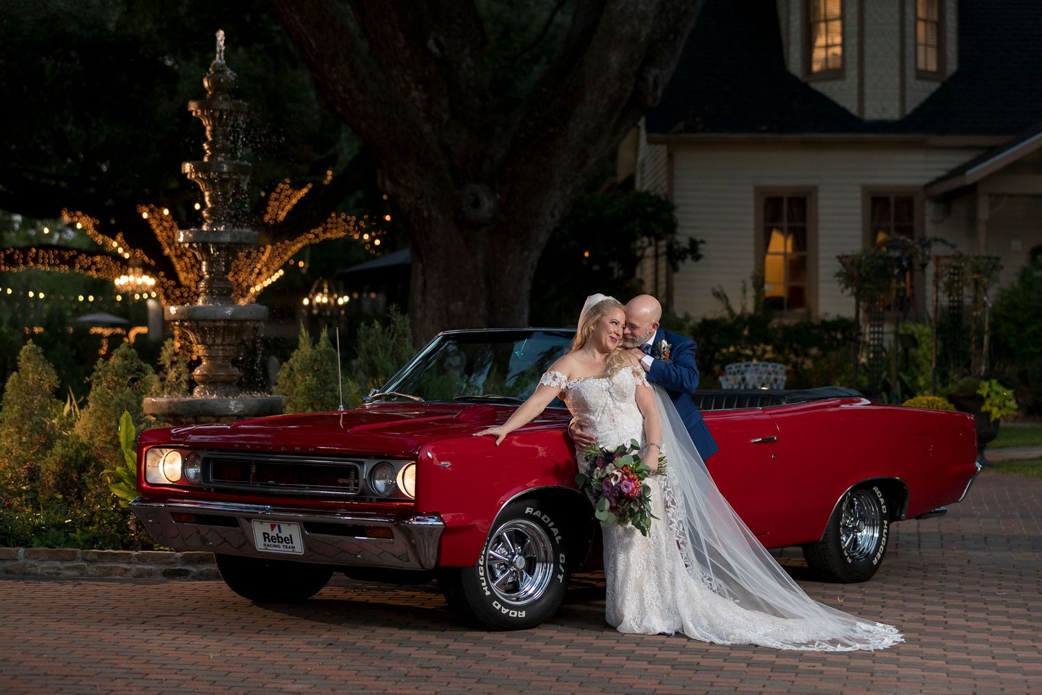 Red classic Chevrolet convertible parked in front of house with twinkling lights at dusk.
