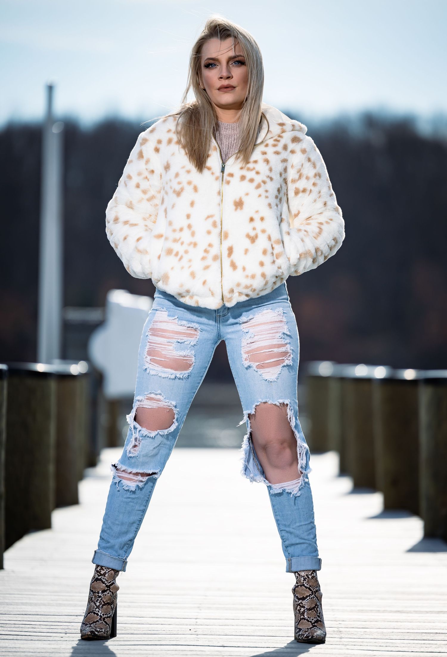Fashion model wearing a leopard print jacket, ripped jeans and animal print boots poses on a wooden deck.