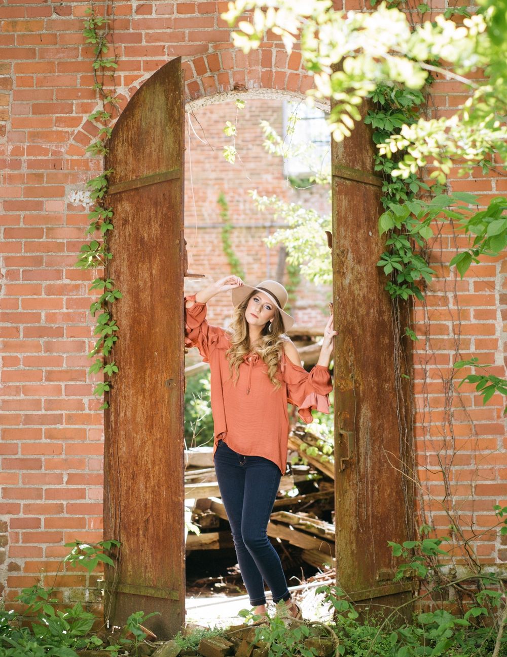 Lifestyle portrait through rustic brick archway with ivy and natural lighting.