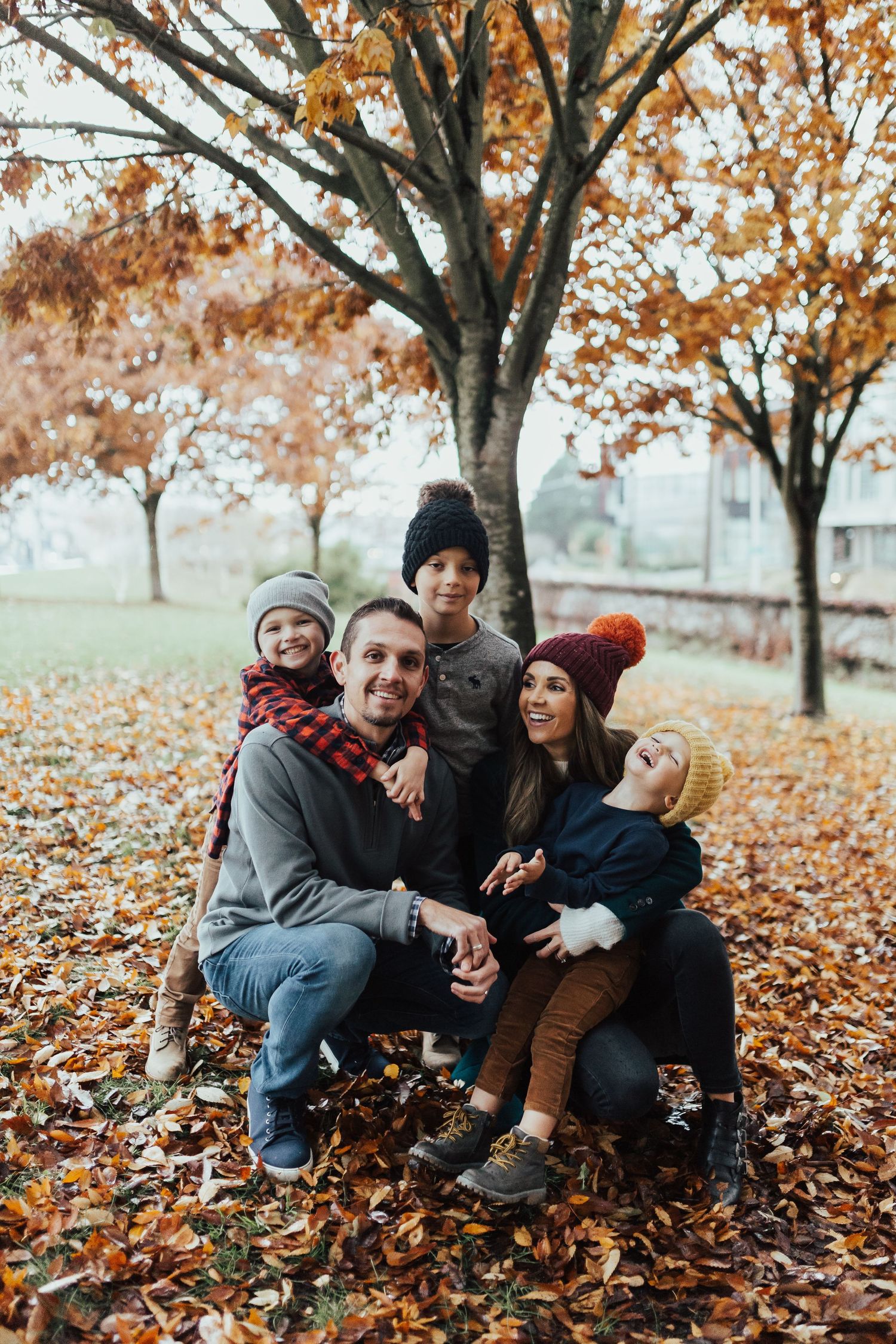 A group sits together on fallen autumn leaves under trees with orange foliage on a misty fall day.