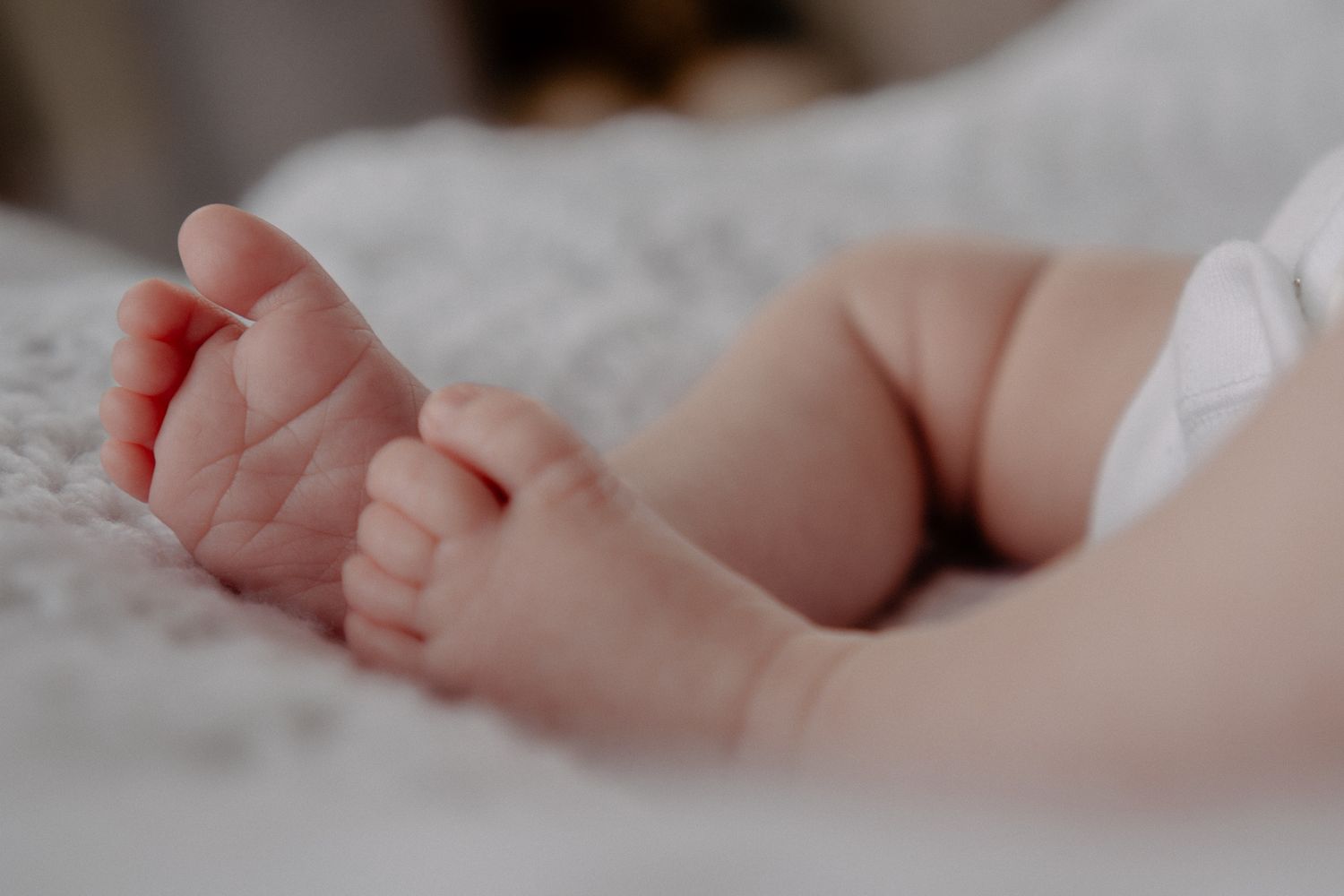 Close-up view of tiny newborn baby feet resting on soft white bedding.