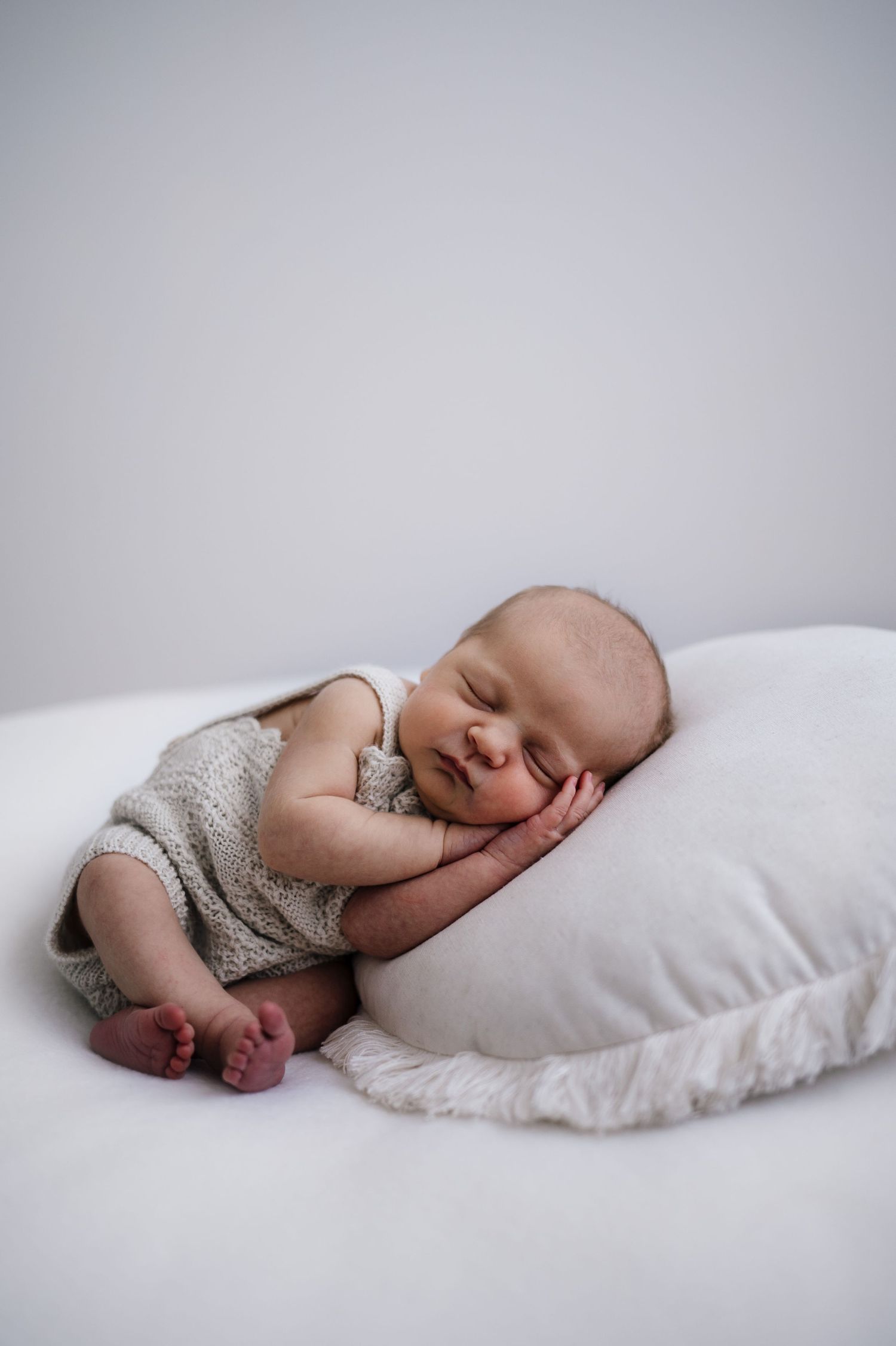 Sleeping baby in gray outfit resting comfortably on white pillow.