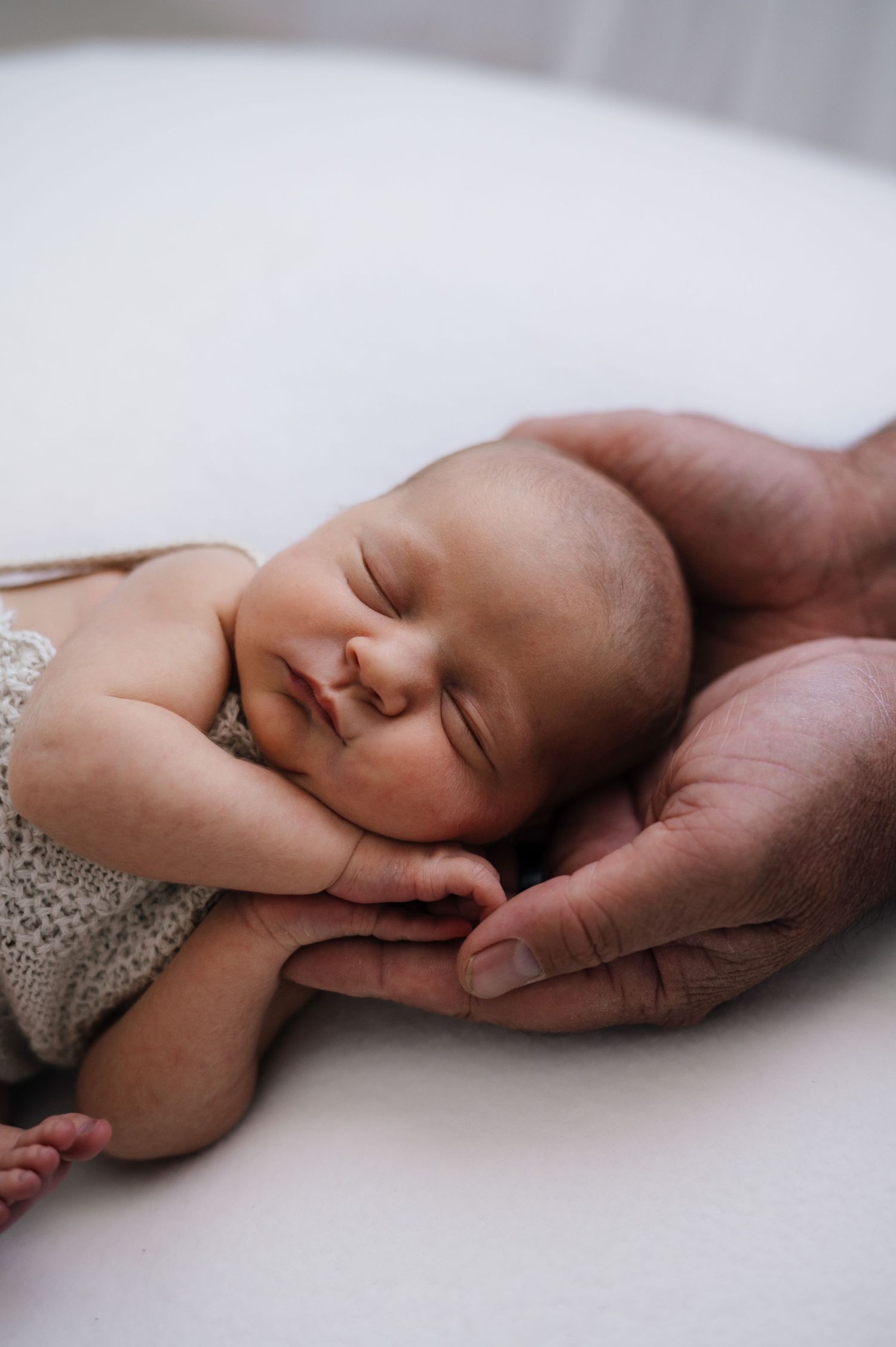Peaceful newborn in lace outfit sleeping while gently supported by hands.