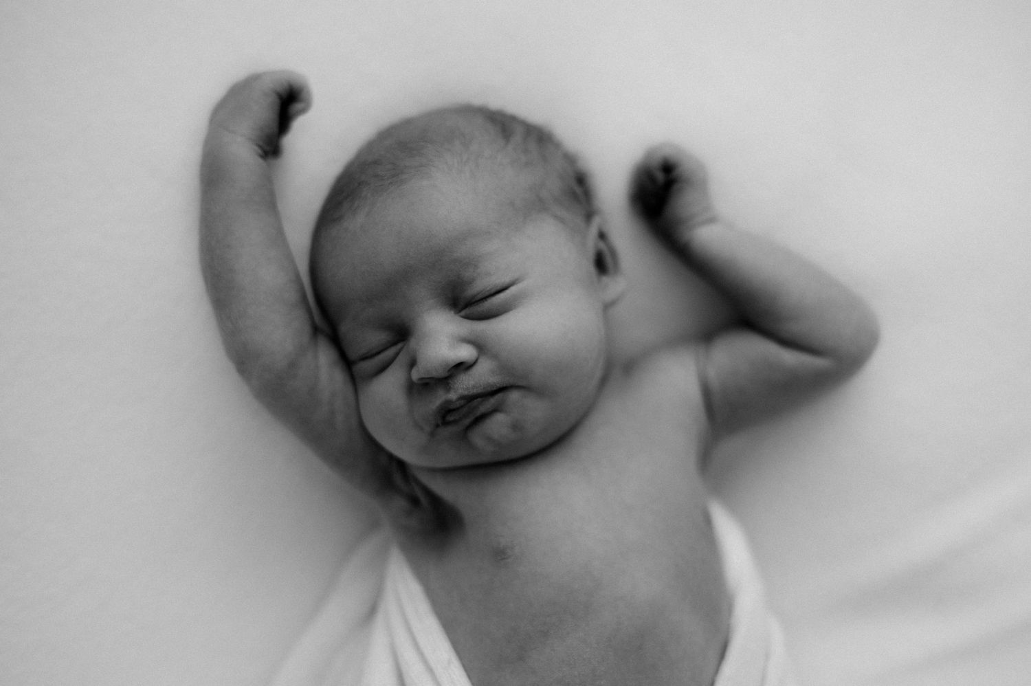 Black and white portrait of sleeping newborn with arms stretched overhead.