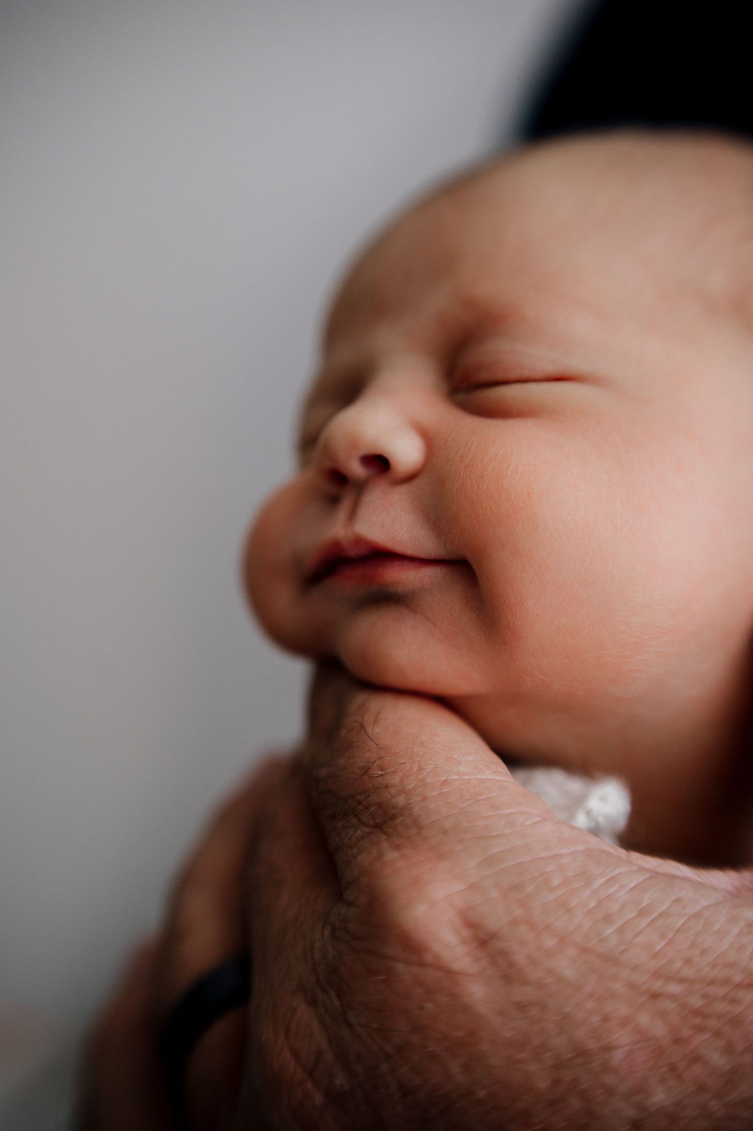Close-up portrait of sleeping newborn supported by gentle hands.