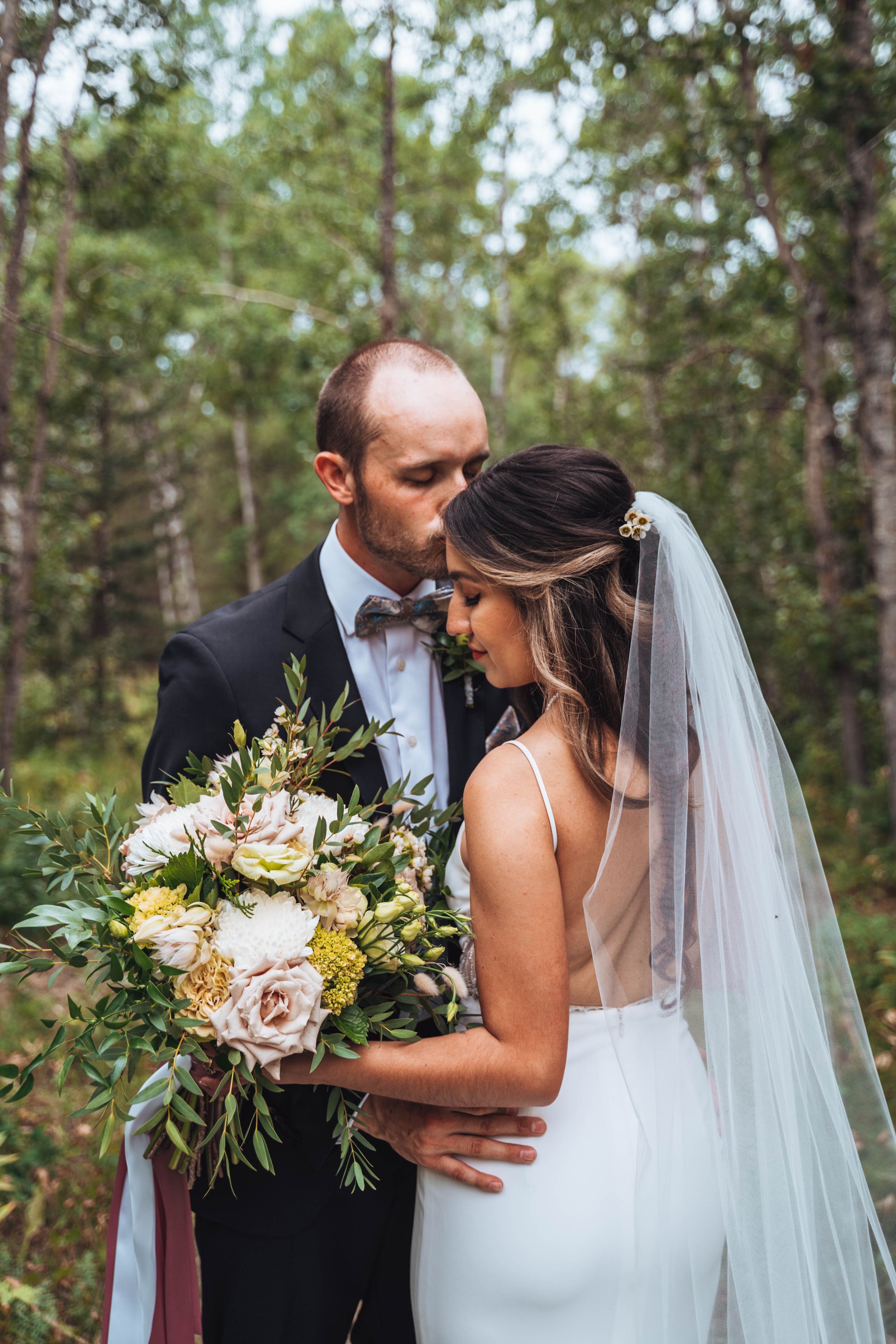 Tender forehead kiss between bride and groom, eyes closed in devotion. Calgary wedding.
