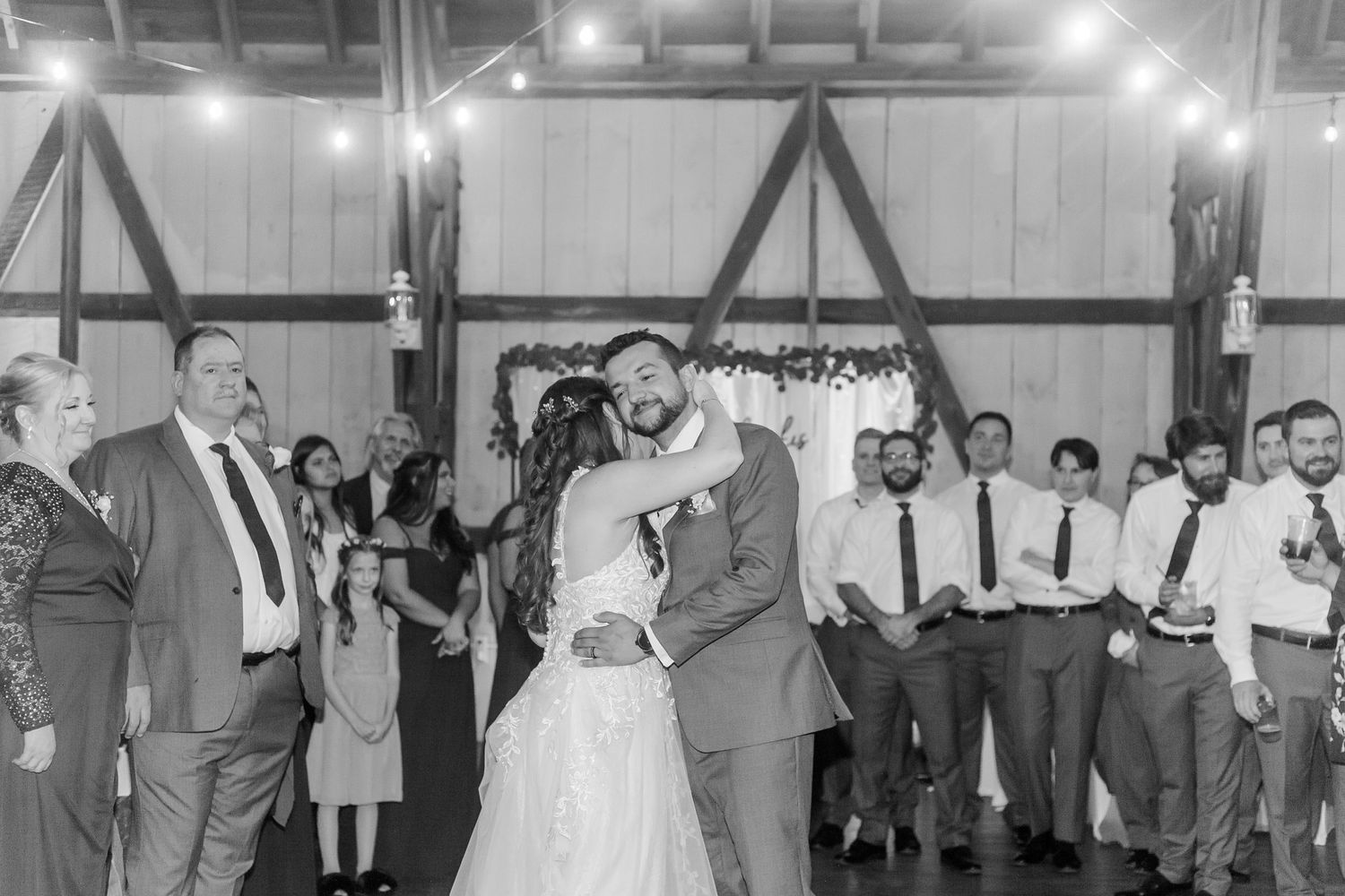 Wedding reception guests dance and celebrate on a wooden dance floor at an indoor venue.