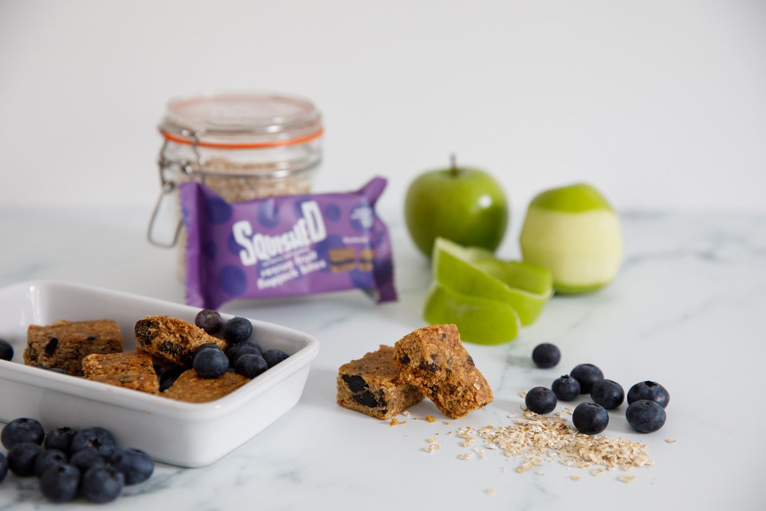 Healthy snack spread with protein bars, fresh fruit, and blueberries on marble surface from a product photoshoot.