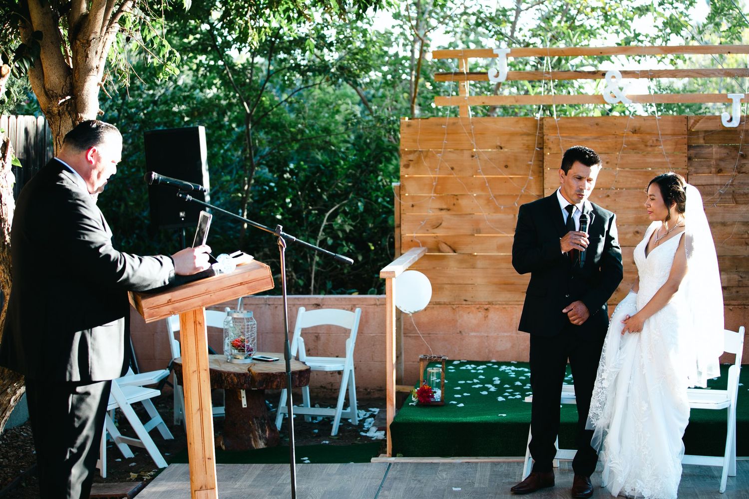 Rustic outdoor wedding ceremony setup with wooden benches and brick wall backdrop.