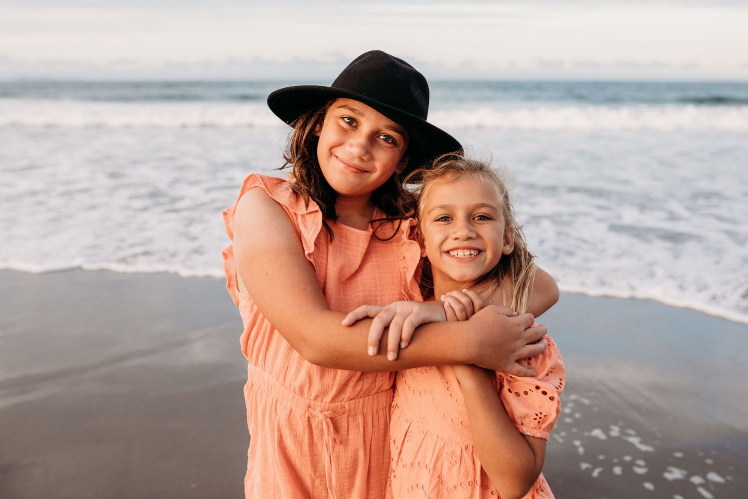 Two people share a joyful embrace on the beach at sunset wearing matching coral outfits.