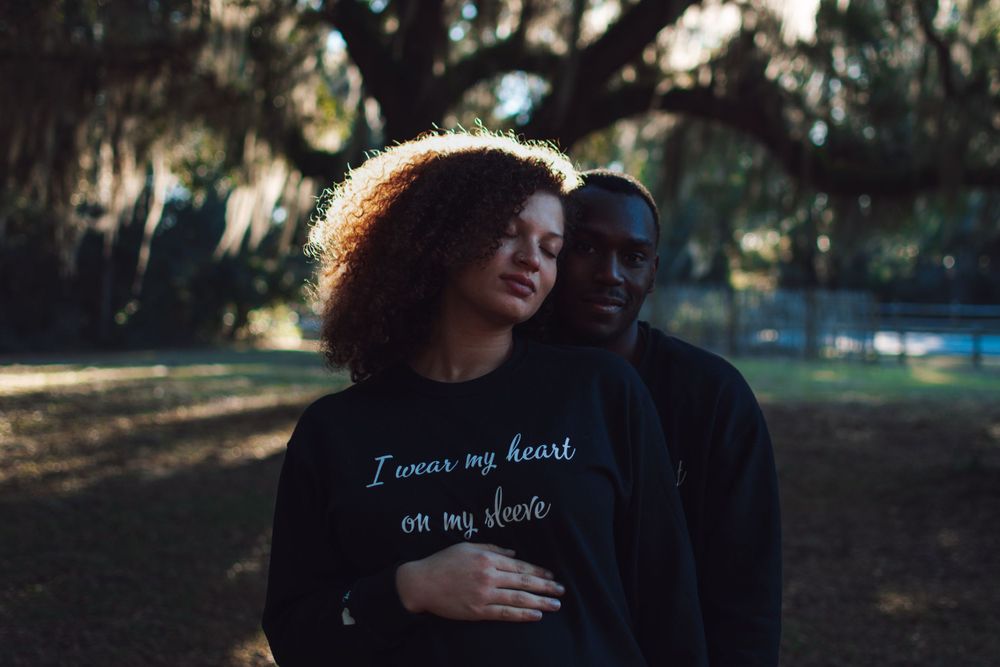 Couple embraces in intimate moment under trees with Spanish moss.