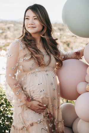 Outdoor maternity photoshoot with pastel balloons and a flowing floral dress.