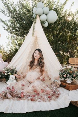 Ethereal maternity portrait in front of a decorated teepee with sage green balloons.