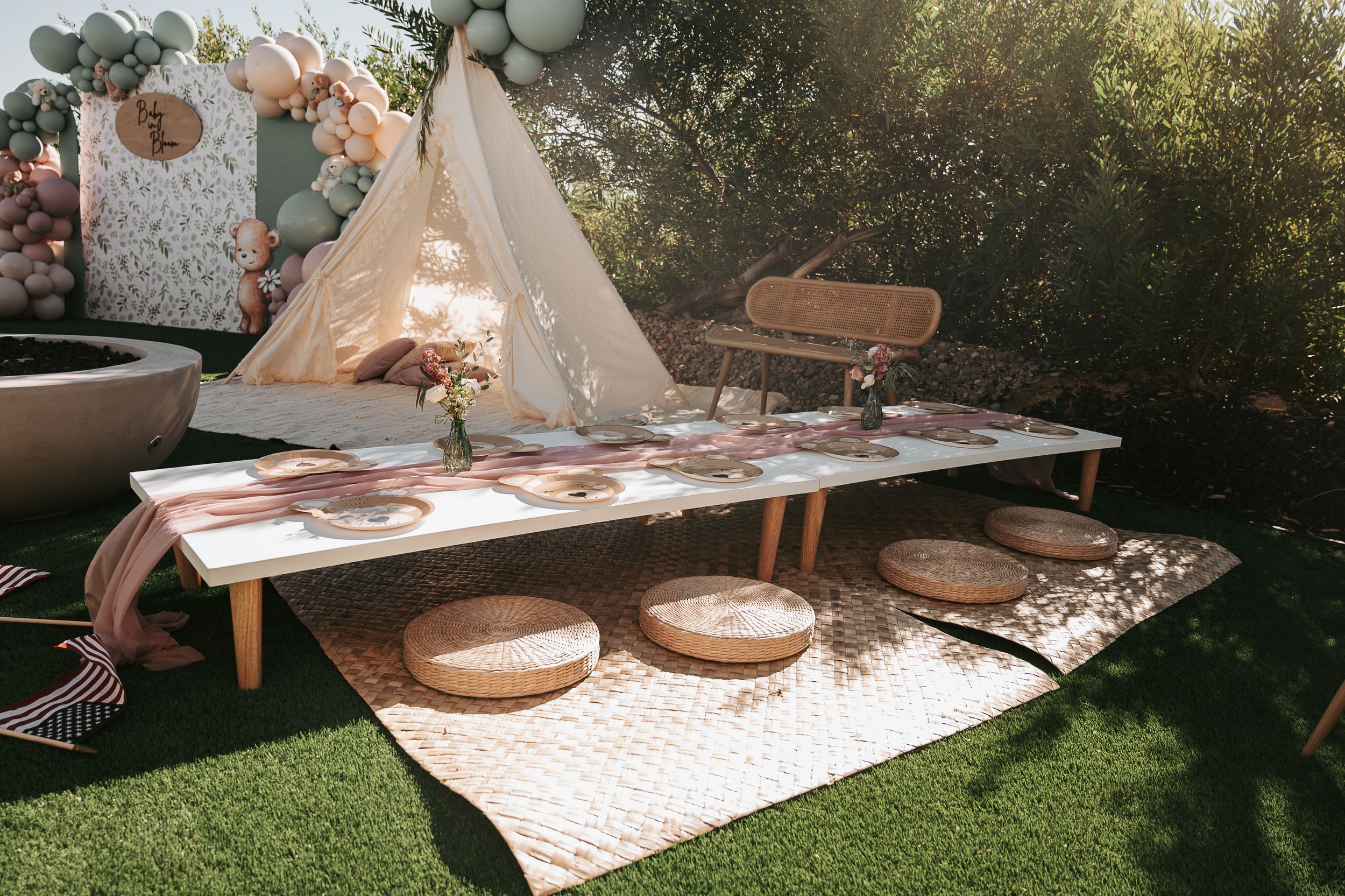 Boho themed baby shower picnic setup with low tables and cushions on white rugs.
