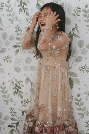 Flowing beige dress with floral details against leafy wallpaper background.
