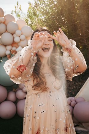 Joyful maternity photo with pastel balloons and a flowing pink floral dress.