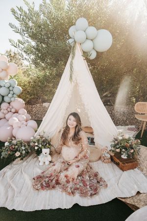 Dreamy maternity photoshoot setup with white teepee, balloons, and floral arrangements.