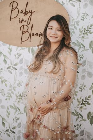 Maternity photo of an expectant mother in a floral dress against a leafy backdrop.
