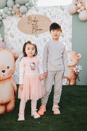 Children posing in front of a baby shower backdrop with teddy bear decorations.