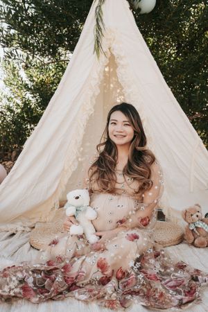 Maternity photo session in front of a white teepee with teddy bears and soft lighting.