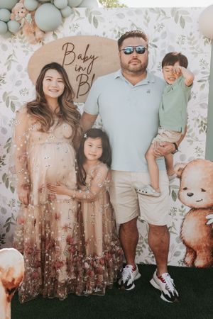 Family photo against floral backdrop with mint green balloons and casual attire.