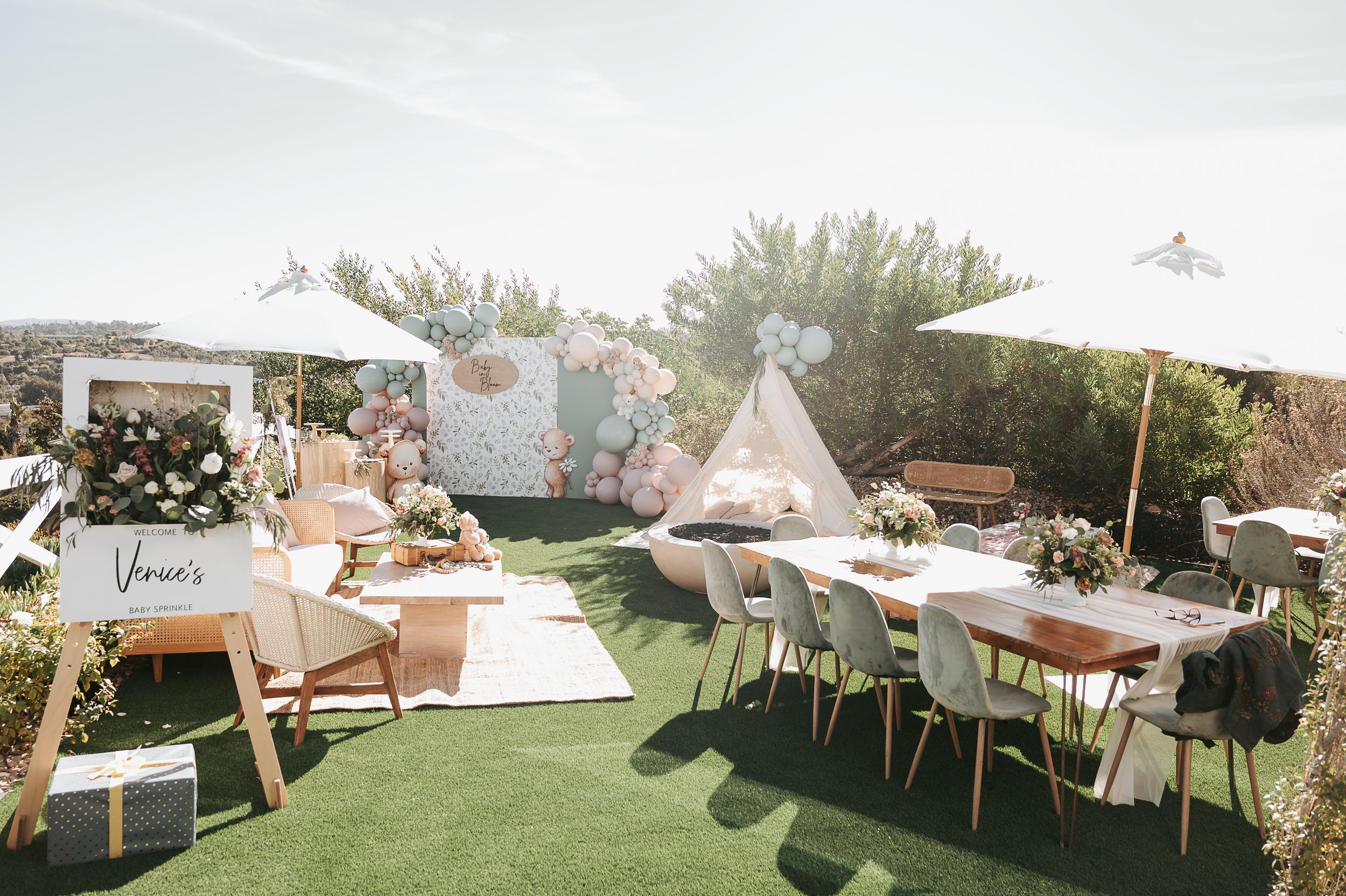 Outdoor baby shower setup with white teepee tents and rustic furniture on grass.