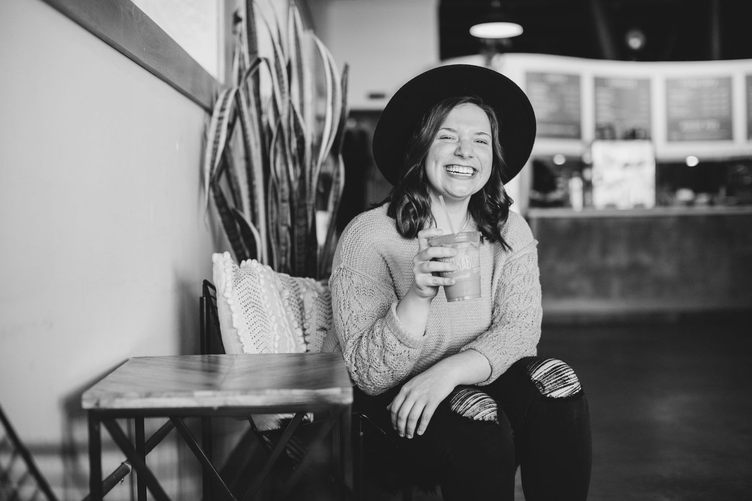 A casual black and white indoor portrait of someone holding a drink at a coffee shop.