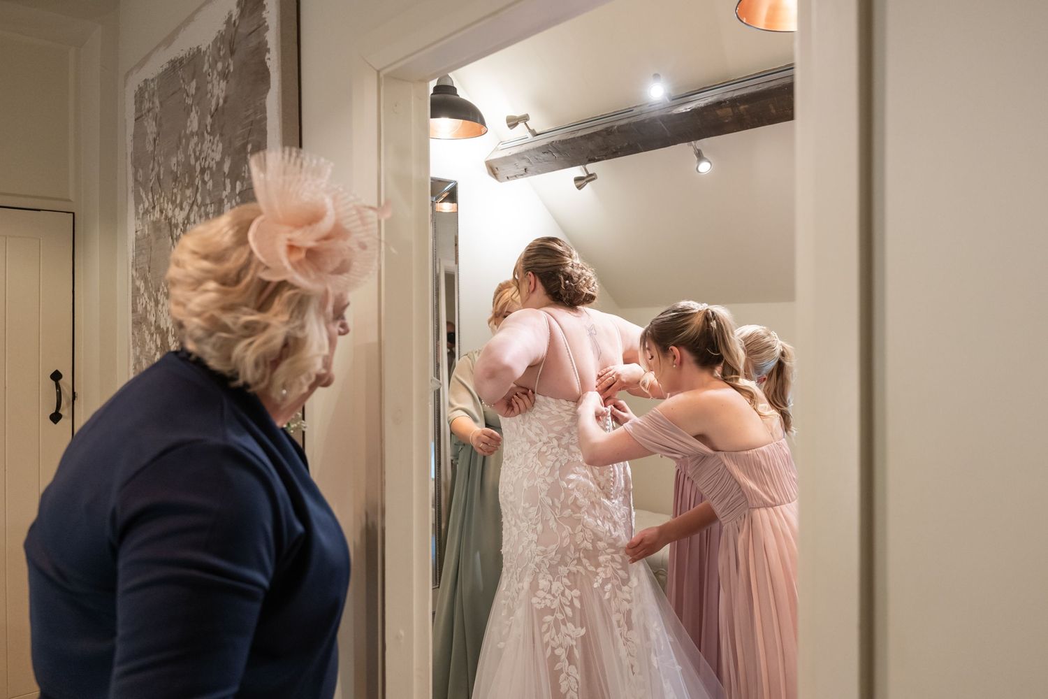 Wedding dress fitting scene with attendants helping adjust the gown.