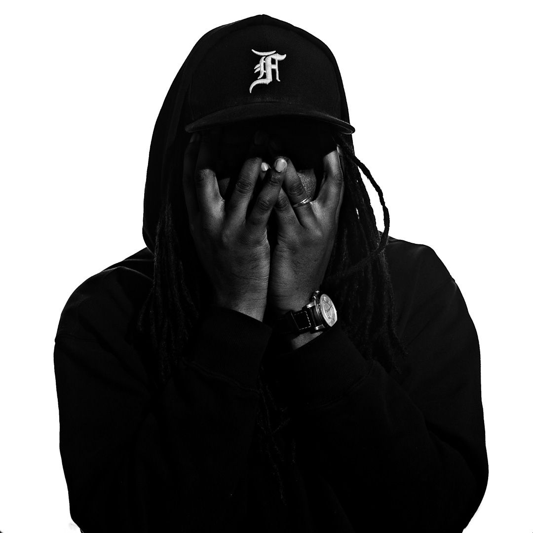 Black and white portrait of someone in a dark hoodie and cap covering their face with their hands.