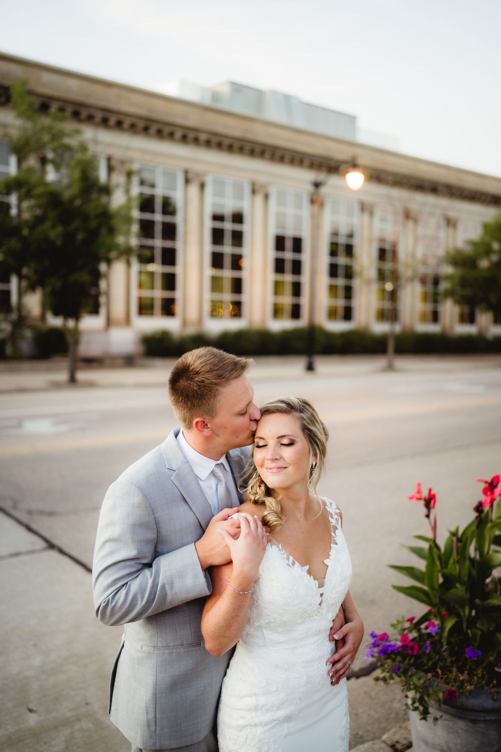 Elegant wedding moment outside historic building with blooming flowers.