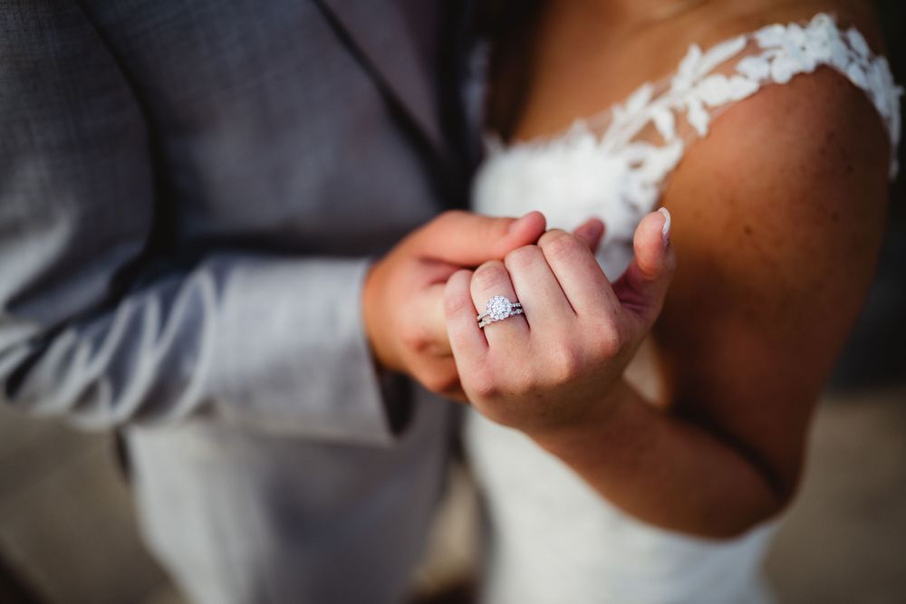 Close-up detail shot of wedding rings and hands with lace dress detail.