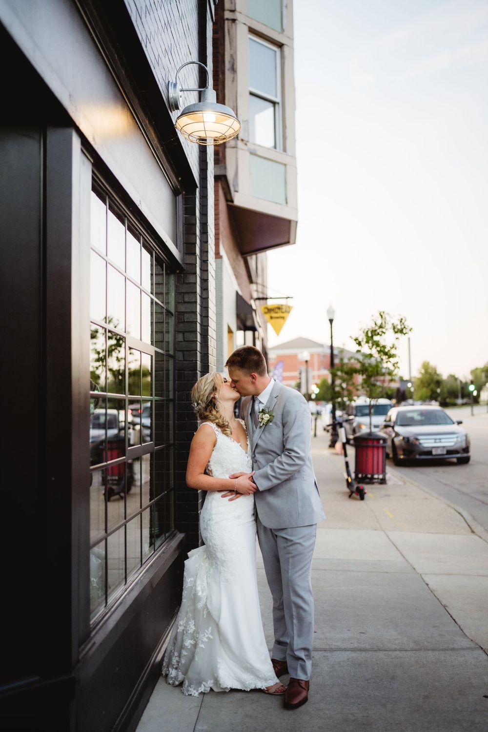A romantic wedding couple shares an intimate moment outside a storefront at dusk.