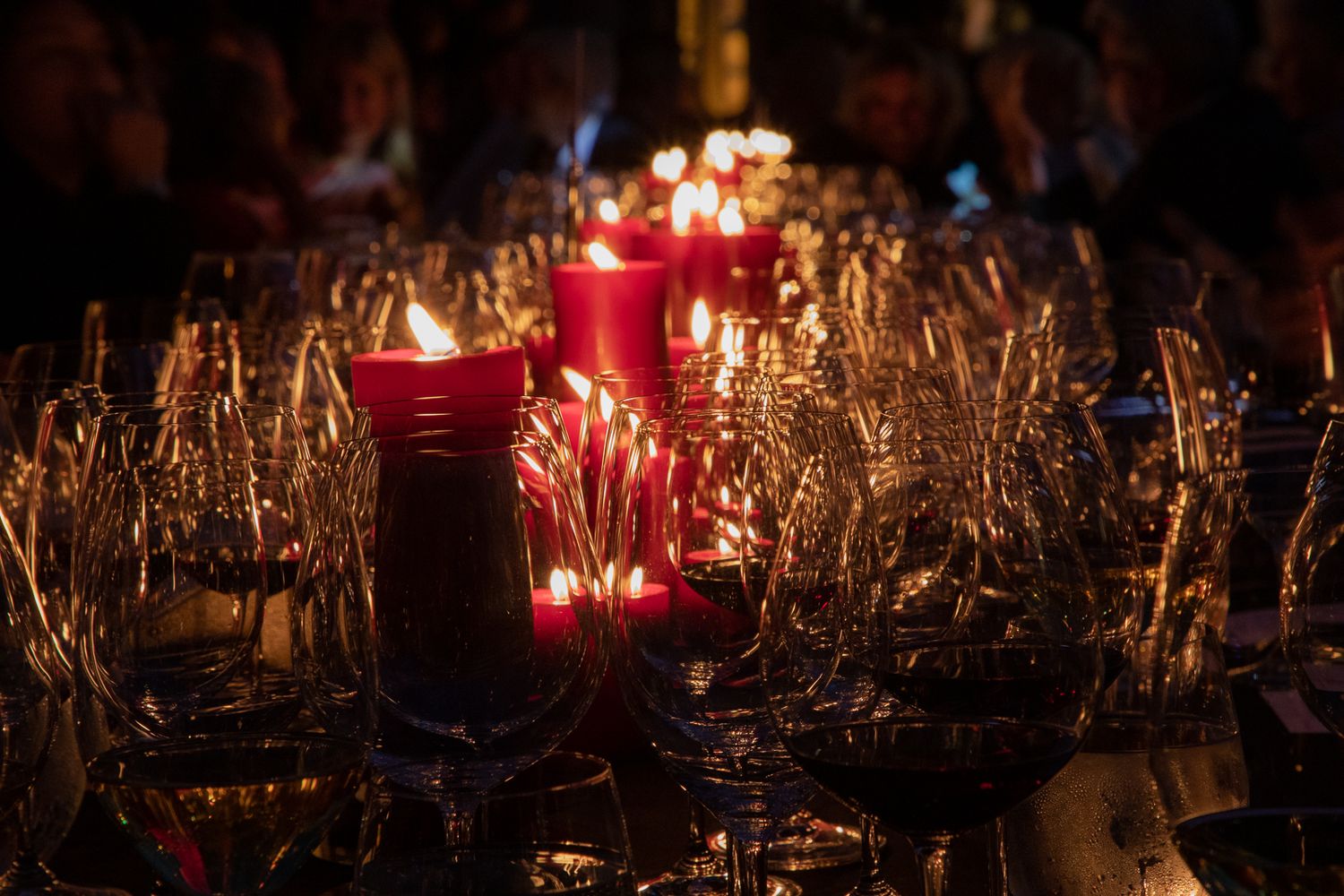 Red glowing candles surrounded by dry wheat stalks and wine glasses create a cozy autumn dining atmosphere.