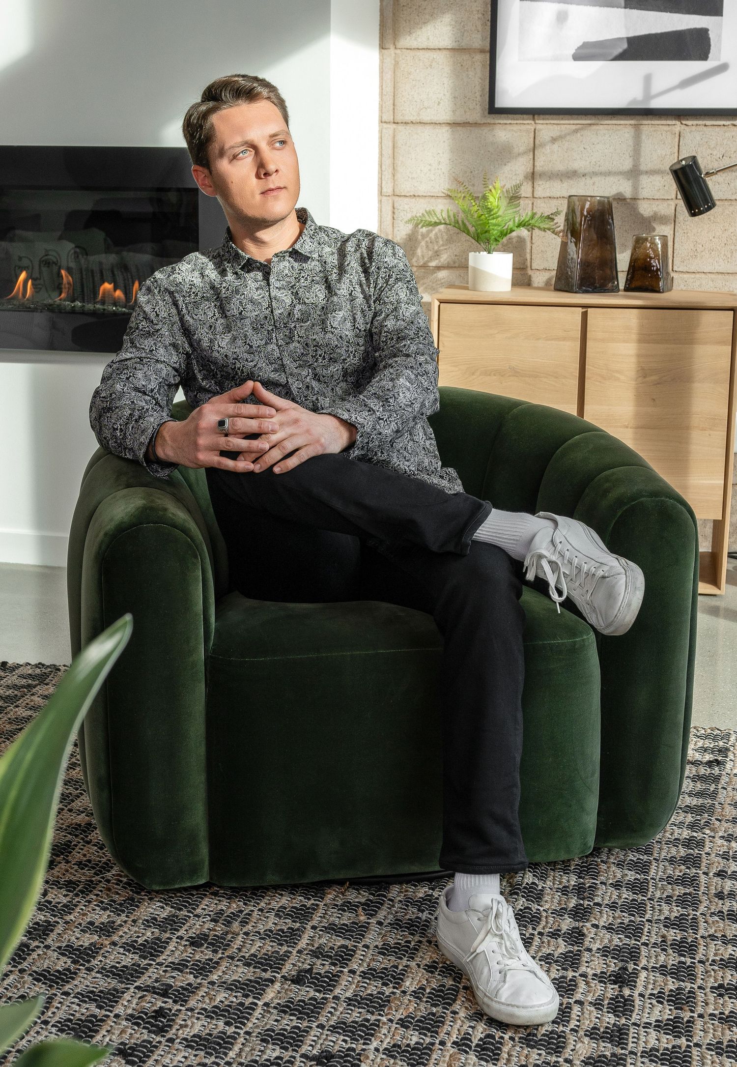 Person lounging on plush green velvet sofa in modern living room with patterned carpet.