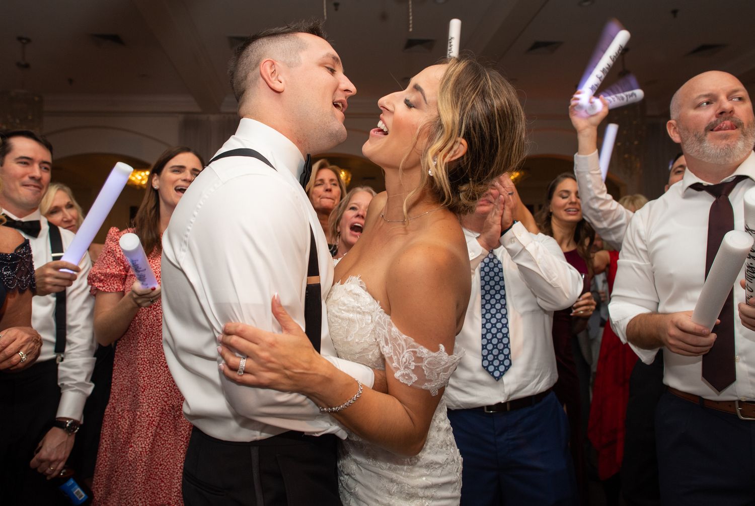 Energetic dance floor moment at wedding reception with light-up foam sticks.